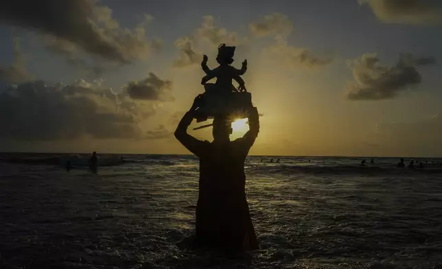 A devotee carries an idol of elephant-headed Hindu god Ganesha on his head to immerse in the Arabian Sea, during the ten days long Ganesh Chaturthi festival in Mumbai, India, Sunday, Sept. 8, 2024. (AP Photo/Rafiq Maqbool)