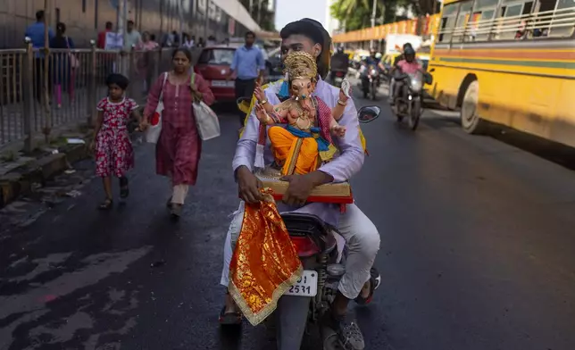 A devotee carries an idol of elephant-headed Hindu god Ganesha to home on a motorcycle for worship during Ganesh Chaturthi festival celebrations in Mumbai, India, Saturday, Sept. 7, 2024. (AP Photo/Rafiq Maqbool)