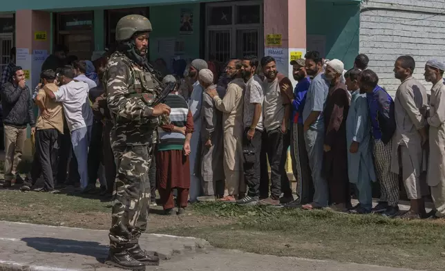 An Indian paramilitary soldier stands guard as people queue up at a polling booth to cast their vote in Bellow, south of Srinagar, Indian controlled Kashmir, Wednesday, Sept. 18, 2024. (AP Photo/Dar Yasin)