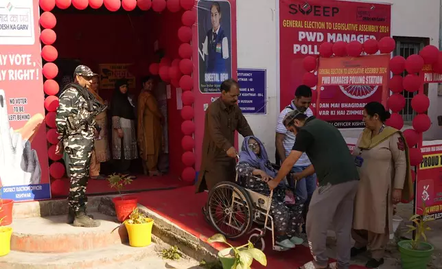 People help an elderly woman in a wheel chair down a ramp after she cast her vote during the first phase of the Jammu and Kashmir Assembly election, in Kishtwar, India, Wednesday, Sept. 18, 2024. (AP Photo/Channi Anand)