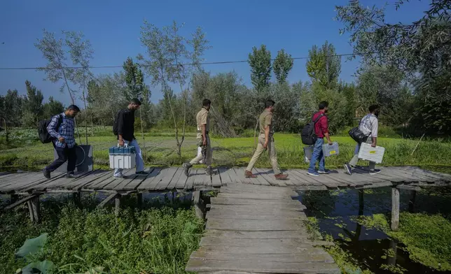 Polling officials and police walk on a wooden bridge towards a polling station in the interior of Dal Lake ahead of the second phase of voting for choosing a local government in Indian-controlled Kashmir, in Srinagar, Tuesday, Sept. 24, 2024. (AP Photo/Mukhtar Khan)