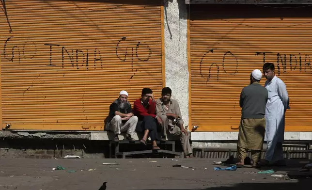 Kashmiris sit outside closed shops painted with graffiti during a curfew in central Srinagar, India, Thursday, Sept. 16, 2010. (AP Photo/Dar Yasin, File)