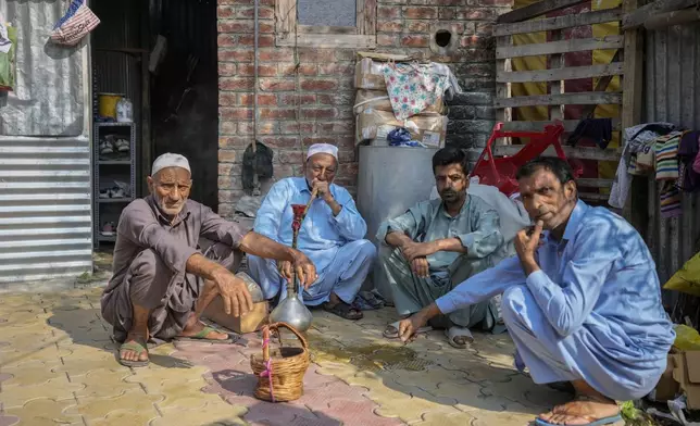 FILE- An elderly man smokes a hookah pipe as he sits with other men outside a polling station during the second phase of the assembly election in the interior of Dal Lake in Srinagar, Indian controlled Kashmir, Sept. 25, 2024.(AP Photo/Mukhtar Khan, File)