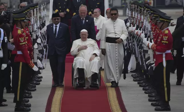 Pope Francis on his wheelchair, is welcomed as Indonesian Minister of Religious Affairs Yaqut Cholil Qoumas, center left, walks during an official welcoming ceremony at Soekarno-Hatta International Airport in Tangerang on the outskirts of Jakarta, Indonesia, Tuesday, Sept. 3, 2024. (AP Photo/Achmad Ibrahim)