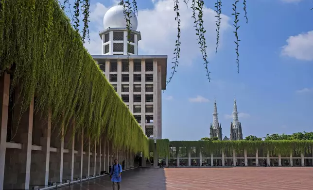 A man walks in the shade at Istiqlal Mosque as the spires of the Our Lady of The Assumption Cathedral are seen in the background, in Jakarta, Indonesia, Friday, Aug. 9, 2024. (AP Photo/Tatan Syuflana)