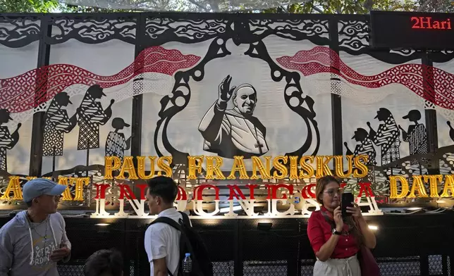 People walk past a welcoming signboard for Pope Francis displayed at Jakarta Cathedral in Jakarta, Indonesia, Sunday, Sept. 1, 2024, ahead of his visit to Indonesia from Sept. 3-6. (AP Photo/Dita Alangkara)