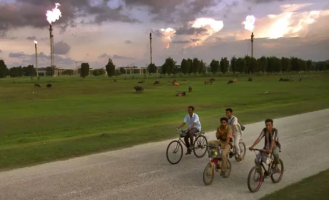 FILE- Acehnese men bicycle to work past an Exxon Mobil gas production facility in Lhokseumawe, Aceh province, Indonesia, April 4, 2001.(AP Photo/Ed Wray, File)