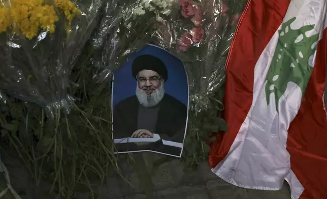 A poster of Hezbollah leader Sayyed Hassan Nasrallah is placed next to bouquets of flowers and Lebanese flag in front of the Lebanese Embassy in Tehran, Iran, Wednesday, Sept. 18, 2024. (AP Photo/Vahid Salemi)