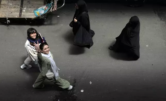 FILE - An Iranian woman without wearing her mandatory Islamic headscarf flashes a victory sign as two head-to-toe veiled women walk at the old main bazaar of Tehran, Iran, June 13, 2024. (AP Photo/Vahid Salemi, File)