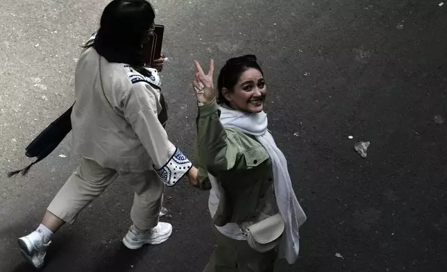 FILE - An Iranian woman without a mandatory headscarf, or hijab, flashes a victory sign as she walks at the old main bazaar of Tehran, Iran, June 13, 2024. (AP Photo/Vahid Salemi, File)