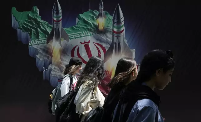 FILE - Iranian women without a mandatory headscarf, or hijab, walk past a banner showing missiles being launched from Iranian map in northern Tehran, Iran, April 19, 2024. (AP Photo/Vahid Salemi, File)