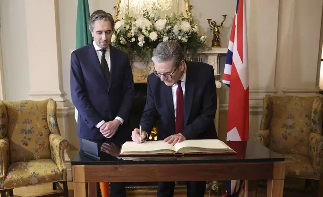 The Prime Minister of Ireland Simon Harris, left watch as his British counterpart Keir Starmer signs the visitors book as they meet for talks at Farmleigh House in Dublin, Ireland, Saturday, Sept. 7, 2024. (AP Photo/Peter Morrison Pool)