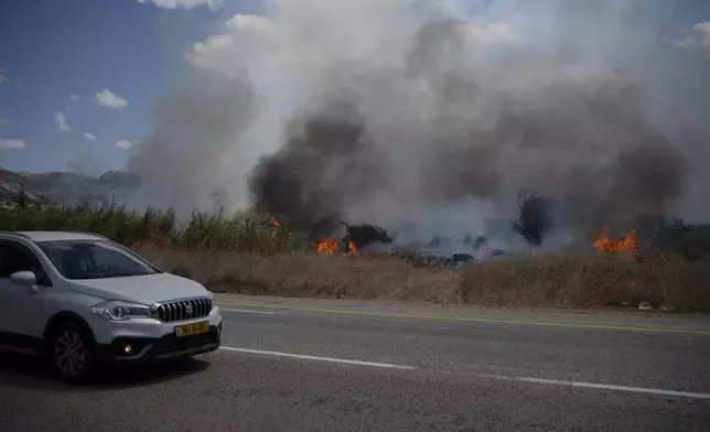 A car drives past fire burning in an area, following an attack from Lebanon, near the Kibbutz Snir, northern Israel, Monday, Sept. 16, 2024. (AP Photo/Leo Correa)