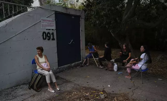 Israelis sit next to a public bomb shelter to stay safe from rockets fired from Lebanon, in Haifa, northern Israel, on Tuesday, Sept. 24, 2024. (AP Photo/Baz Ratner)