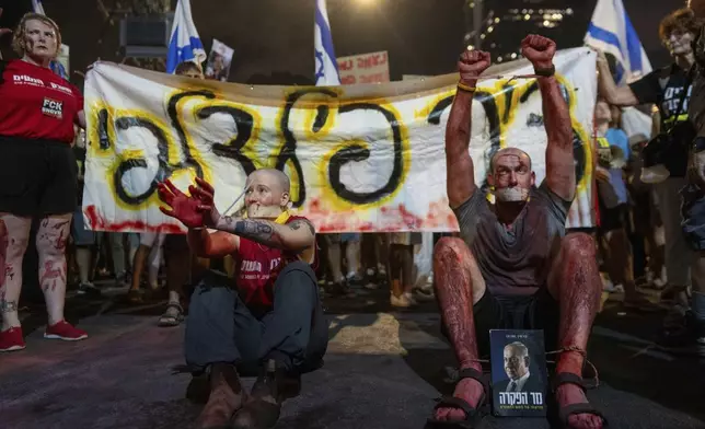 An activist wears theatrical blood, bound wrists and his mouth taped as relatives of hostages held by Hamas militants in the Gaza Strip and their supporters call for their immediate release and to protest against Prime Minister Benjamin Netanyahu's government in Tel Aviv, Israel, Saturday, Aug. 31, 2024. (AP Photo/Ohad Zwigenberg)