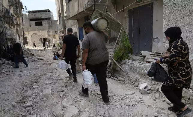 Palestinian refugees walk through the rubble of destroyed houses while they flee their homes during the Israeli army operation in the West Bank refugee camp of Tulkarem, in Tulkarem, Thursday, Sept. 5, 2024. (AP Photo/Nasser Nasser)