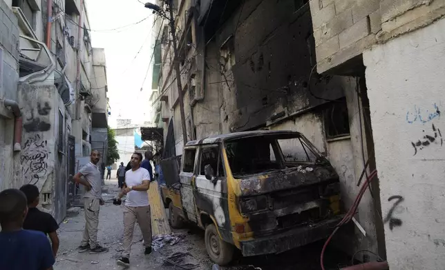 Palestinian refugees inspect a burnt vehicle in a West Bank refugee camp in Tulkarem, during an Israeli army operation in Tulkarem, Thursday, Sept. 12, 2024. (AP Photo/Nasser Nasser)