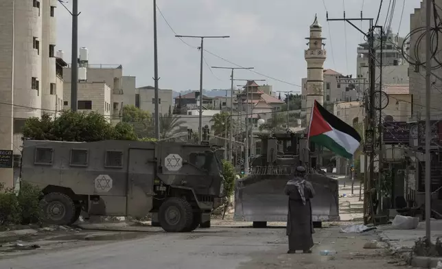 Palestinian activist Khairi Hanoon waves the Palestinian flag as a convoy of Israeli military armored vehicles drives by during an army raid in Tulkarem, West Bank, on Tuesday, Sept. 3, 2024. (AP Photo/Majdi Mohammed)