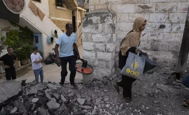 Palestinian refugees walk through a damaged road while they flee their homes during the Israeli army operation in the West Bank refugee camp of Tulkarem, in Tulkarem, Thursday, Sept. 5, 2024. (AP Photo/Nasser Nasser)