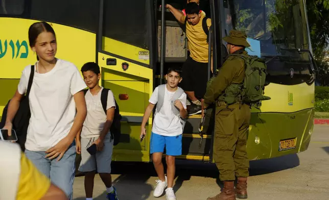 An Israeli soldier stands next to a bus as students arrive at their elementary school on the first day of classes near the kibbutz Magen, located on an area near the border with Gaza Strip, southern Israel, Sunday, Sept. 1, 2024. (AP Photo/Tsafrir Abayov)