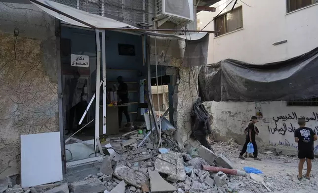 Palestinian refugees walk past rubble of a partly destroyed shop in the West Bank refugee camp of Tulkarem, during an Israeli army operation in Tulkarem, Thursday, Sept. 12, 2024. (AP Photo/Nasser Nasser)