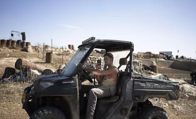 An Israeli settler films Palestinian residents and activists in the West Bank village of Khirbet Zanuta, Thursday, Aug. 29, 2024. Ten months after settlers threatened to kill them if they didn't leave their village, some Palestinian residents are finally home, under a rare court order. (AP Photo/Maya Alleruzzo)