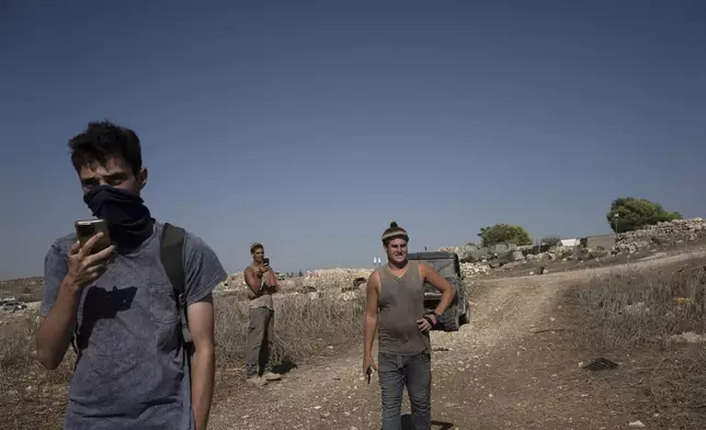 An Israeli activist, left, calls Israeli Police as settlers visit the West Bank village of Khirbet Zanuta, Thursday, Aug. 29, 2024. Ten months after settlers threatened to kill them if they didn't leave their village, some Palestinian residents are finally home, under a rare court order. (AP Photo/Maya Alleruzzo)