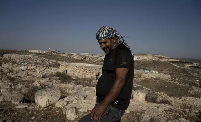 Hassan Battat stands in the West Bank village of Khirbet Zanuta, near his home, rear left, overlooking the Meitarim settlement, Thursday, Aug. 29, 2024. Ten months after settlers threatened to kill them if they didn't leave this village, some Palestinian residents are finally home, under a rare court order. (AP Photo/Maya Alleruzzo)