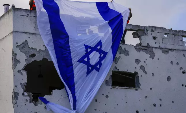 Municipality workers hang an Israeli flag over a damaged building that was hit by a rocket fired from Lebanon, in Kiryat Bialik, northern Israel, on Sunday, Sept. 22, 2024. (AP Photo//Ariel Schalit)