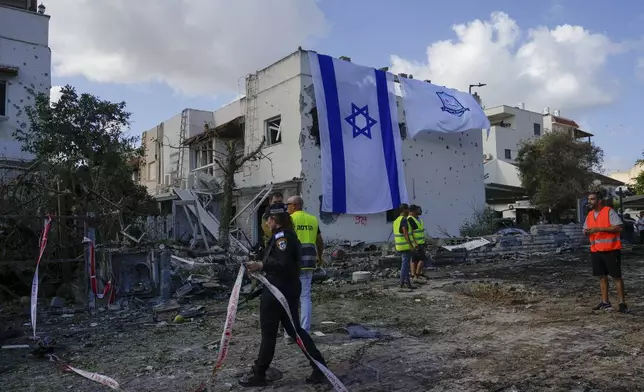 Municipality workers hang an Israeli flag over a damaged building that was hit by a rocket fired from Lebanon, in Kiryat Bialik, northern Israel, on Sunday, Sept. 22, 2024. (AP Photo//Ariel Schalit)