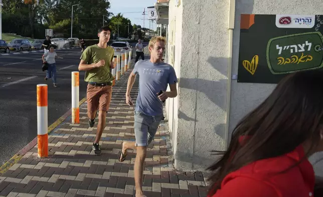 Israelis run to take cover as a siren sounds a warning of incoming rockets fired from Lebanon, in Nahariya, northern Israel, Thursday, Sept. 19, 2024. (AP Photo/Baz Ratner)