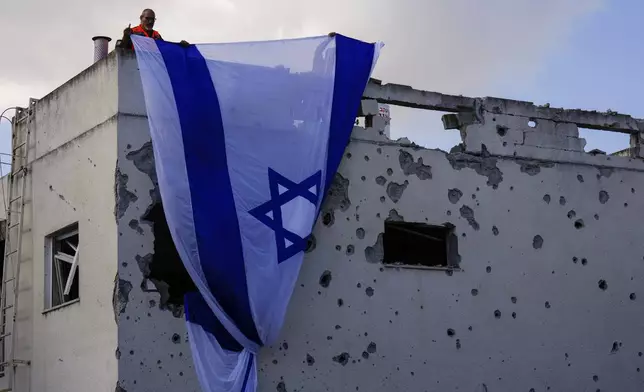 Municipality workers hang an Israeli flag over a damaged building that was hit by a rocket fired from Lebanon, in Kiryat Bialik, northern Israel, on Sunday, Sept. 22, 2024. (AP Photo//Ariel Schalit)