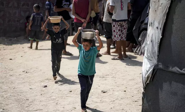 Palestinian children collect food aid at a makeshift tent camp in Deir al-Balah, central Gaza Strip, Thursday, Aug. 29, 2024. (AP Photo/Abdel Kareem Hana)