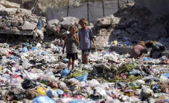 Displaced kids sort through trash at a street in Deir al-Balah, central Gaza Strip, Thursday, Aug. 29, 2024. (AP Photo/Abdel Kareem Hana)