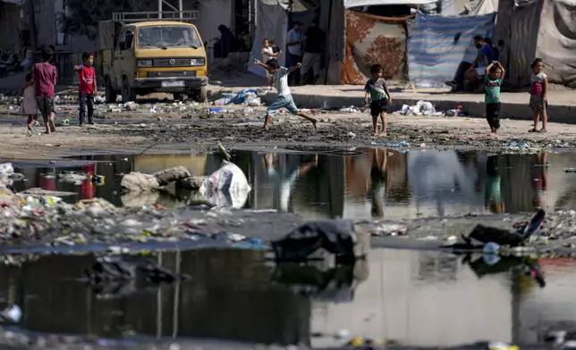 Displaced children walk through a dark streak of sewage flowing into the streets of Deir al-Balah, central Gaza Strip, Thursday, Aug. 29, 2024. (AP Photo/Abdel Kareem Hana)