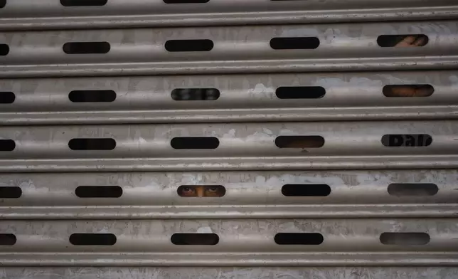 A Palestinian youth watches through a locked fence from inside a shopping mall during a military raid in Jenin, West Bank, Thursday, June 6, 2024. (AP Photo/Bram Janssen)