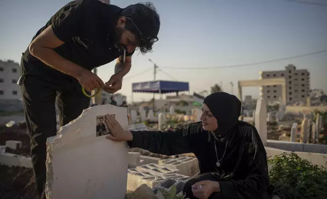 Amjad Hamadneh tapes a photograph to the grave of his son, Mahmoud, as the teen’s mother looks on, in Jenin, West Bank, Wednesday, June 5, 2024. Witnesses said Mahmoud, 15, was killed by an Israeli sniper on his way home from school. (AP Photo/Bram Janssen)