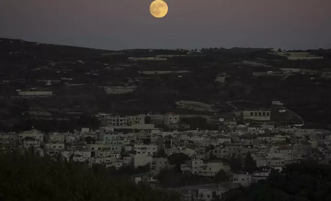 The supermoon rises behind the houses in Mas'ade, a village in the Israeli-annexed Golan Heights, Tuesday, Sept. 17, 2024. (AP Photo/Leo Correa)