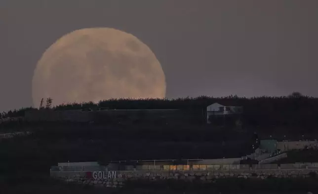 The supermoon rises behind a house in Mas'ade, a village in the Israeli-annexed Golan Heights, Tuesday, Sept. 17, 2024. (AP Photo/Leo Correa)