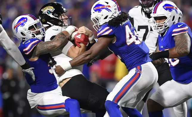 Jacksonville Jaguars quarterback Trevor Lawrence, center, is sacked by Buffalo Bills defensive end AJ Epenesa, left, and linebacker Dorian Williams (42) during the second half of an NFL football game Monday, Sept. 23, 2024, in Orchard Park, NY. (AP Photo/Adrian Kraus)