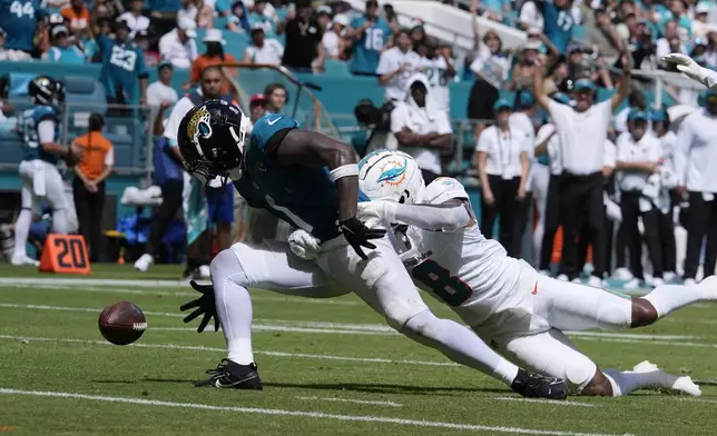 Miami Dolphins safety Jevon Holland (8) grabs Jacksonville Jaguars running back Travis Etienne Jr. (1) as he fumbles the ball during the second half of an NFL football game, Sunday, Sept. 8, 2024, in Miami Gardens, Fla. (AP Photo/Rebecca Blackwell)