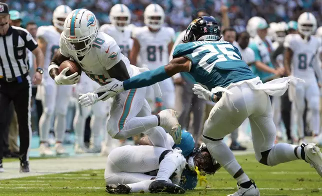 Jacksonville Jaguars cornerback Jarrian Jones (22) and safety Antonio Johnson (26) attempt to stop Miami Dolphins wide receiver Tyreek Hill (10) during the first half of an NFL football game, Sunday, Sept. 8, 2024, in Miami Gardens, Fla. (AP Photo/Rebecca Blackwell)