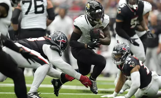 Jacksonville Jaguars running back Travis Etienne Jr., center, runs past Houston Texans defensive tackle Tim Settle Jr., left, during the second half of an NFL football game, Sunday, Sept. 29, 2024, in Houston. (AP Photo/Eric Gay)