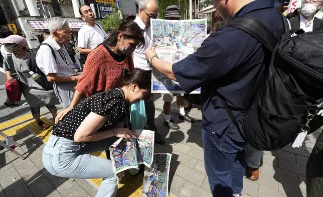 Pedestrians try to obtain an extra edition of the Sports Hochi newspaper reporting on the Los Angeles Dodgers' Shohei Ohtani becoming the first player in major league history with 50 home runs and 50 stolen bases in a season, Friday, Sept. 20, 2024, in Tokyo. (AP Photo/Eugene Hoshiko)