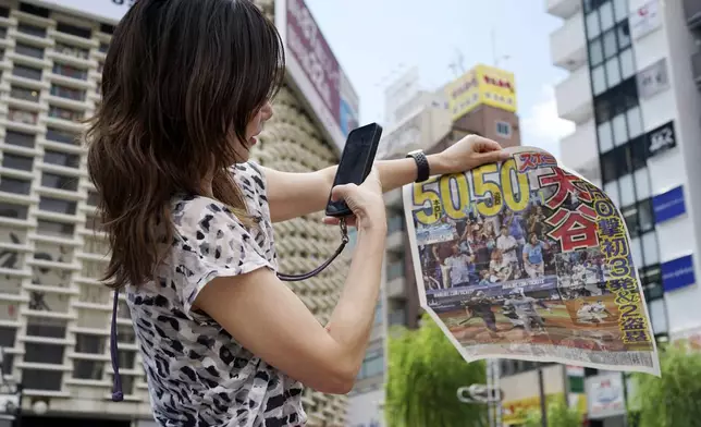 A pedestrian takes a photo of an extra edition of the Sports Nippon newspaper reporting on the Los Angeles Dodgers' Shohei Ohtani becoming the first player in major league history with 50 home runs and 50 stolen bases in a season, Friday, Sept. 20, 2024, in Tokyo. (AP Photo/Eugene Hoshiko)