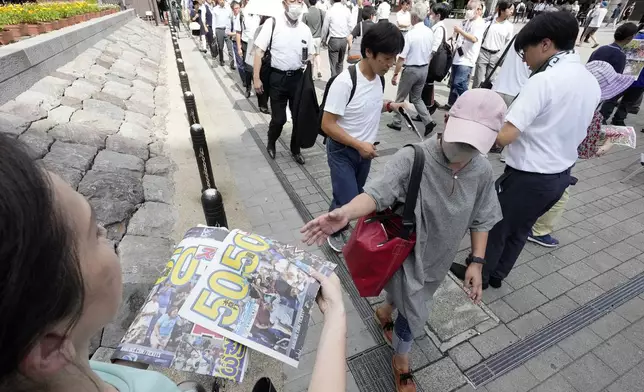 Pedestrians line up to obtain an extra edition of the Sports Nippon newspaper reporting on the Los Angeles Dodgers' Shohei Ohtani becoming the first player in major league history with 50 home runs and 50 stolen bases in a season, Friday, Sept. 20, 2024, in Tokyo. (AP Photo/Eugene Hoshiko)