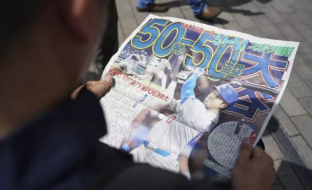 A pedestrian reads an extra edition of the Sports Hochi newspaper reporting on the Los Angeles Dodgers' Shohei Ohtani becoming the first player in major league history with 50 home runs and 50 stolen bases in a season, Friday, Sept. 20, 2024, in Tokyo. (AP Photo/Eugene Hoshiko)