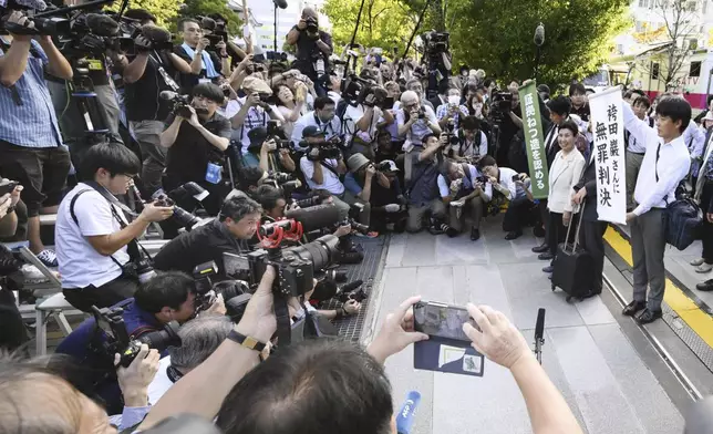 Hideko Hakamada, center at right side, sister of 88-year-old former boxer Iwao Hakamada who has been on death row for nearly six decades after his murder conviction that his lawyers said was based on forced confession and fabricated evidence, is surrounded by journalists after a court ruled that her brother was not guilty in a retrial for a 1966 quadruple murder, in front of the court in Hamamatsu, Shizuoka prefecture, Thursday, Sept. 26, 2024. The signs read "Acquittal to Mr. Iwao Hakamada, " right, and "Acknowledged fabrications of evidence." (Kyodo News via AP)