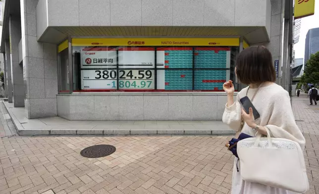 A woman looks at monitors showing Japan's Nikkei 225 index at a securities firm as she waits at an traffic intersection in Tokyo, Monday, Sept. 30, 2024. (AP Photo/Hiro Komae)