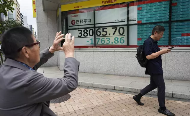 A man who called himself a trader takes a picture of monitors showing Japan's Nikkei 225 index at a securities firm in Tokyo, Monday, Sept. 30, 2024. (AP Photo/Hiro Komae)